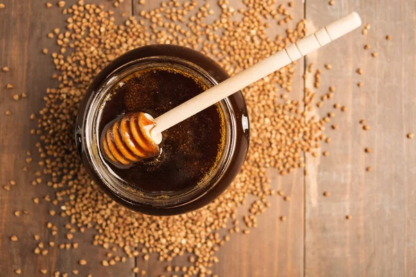 Dark honey with buckwheat over wooden background