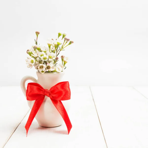 Jarrón blanco con flores pequeñas sobre fondo blanco de madera — Foto de Stock