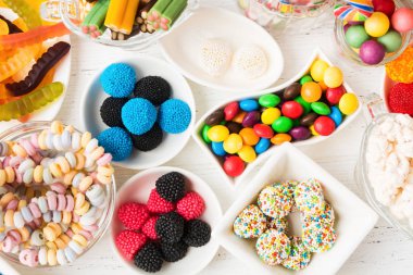 Farklı renklerde tatlılar. Sağlıksız şeker, beyaz ahşap arka planda yiyecek.