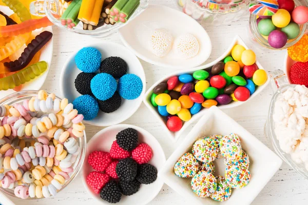 Diferentes dulces de colores. Alimento de caramelos poco saludables sobre fondo de madera blanca —  Fotos de Stock