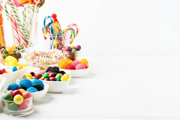 Diferentes dulces de colores. Mezcla dulces en frascos sobre fondo blanco de madera con espacio para copiar —  Fotos de Stock