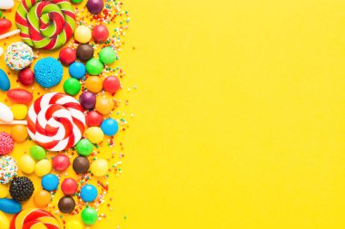 Sarı arka planda renkli şekerler. Üst Manzara. Düz yatıyordu