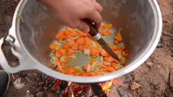 Mężczyzna Nożem Miesza Siekaną Marchewkę Cebulę Garnku Który Wisi Nad — Wideo stockowe