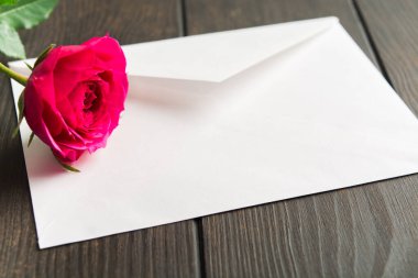Beyaz zarfın üzerinde duran güzel pembe bir gül. Aşk mektubunda romantik bir işaret.