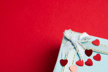 Part of elegant blue gift box with red confetti of heart shape on red background