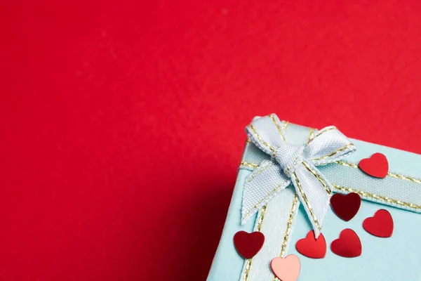 Parte de la elegante caja de regalo azul con confeti rojo de forma de corazón sobre fondo rojo — Foto de Stock