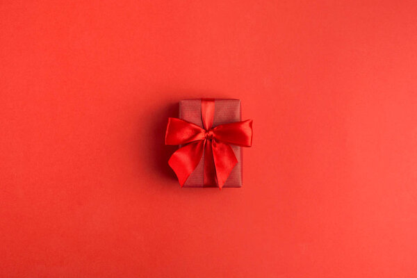 Red gift box in center on red background for womans holiday. February 14, Valentine's day. 8 March, International Women's Day. Flat lay with copy space. Top view