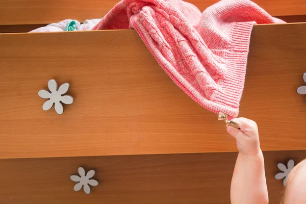 Küçük bebeğin eli açık ahşap şifoniyerden sıcak pembe bir ceket çıkarır. Annenin evde küçük çocuklarla geçirdiği günlük hayatı. Annelik konsepti. Çocuklar yüzünden bir şeyler karıştırıyorsun.