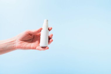 Üzerinde sprey sprey bulunan plastik bir şişe kadın eli mavi arka planda. Boşluğu kopyala
