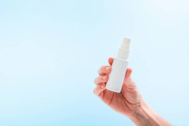 Beyaz plastik şişe tutan kadın elinde virüsü önlemek için sprey ya da mavi arka planda tazelik için su var. Boşluğu kopyala