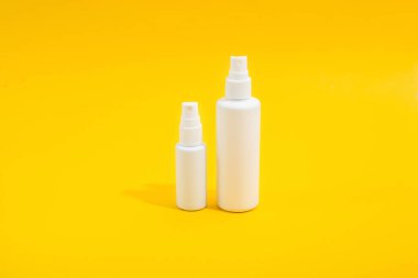 Sarı arka planda spreyi olan iki beyaz plastik şişe. Ev için dezenfektan ve el çantası için mini versiyon. Uzayı kopyala Tasarım için model