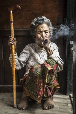 Kathmandu, Nepal - 09 Ağustos 2017: Elinde bastonuyla sigara içen yaşlı bir kadının portresi.