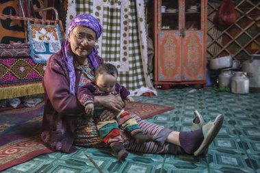 Gobi Çölü, Moğolistan - 29 Temmuz 2017: Renkli giysiler içinde renkli bir mutfakta torunuyla geleneksel bir Moğol büyükannesinin portresi.
