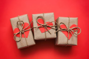 Romantik hediyeler hazır. Kahverengi el işi kağıt ve kenevir ipine sarılı hediye kutuları. Karton kalpler. Kırmızı, sağlam bir arka plan. Paketleri teslim ettim. Sevgililer Günü.