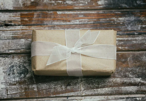ギフトボックスは茶色のクラフト紙に包まれ 白いサテンリボンを結びます クリスマス気分 装飾的な木の背景 現在のパッケージ — ストック写真