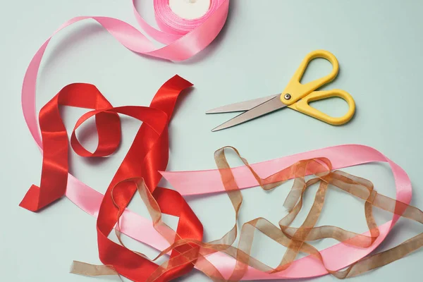 Process of wrapping gift box. Decorative paper, satin ribbons, scissors. Light blue background. Gift shop.