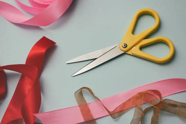 Process of wrapping gift box. Decorative paper, satin ribbons, scissors. Light blue background. Gift shop.