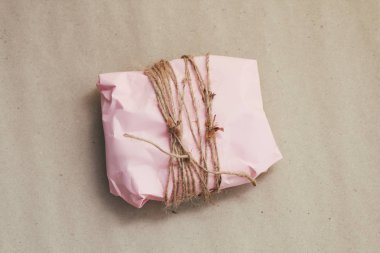 Pembe el işi kağıdına sarılı hediye kutusu ve kahverengi ip. Noel havası. Buruşuk kahverengi arka plan. Hediye paketi. Teslimat servisi. Yumuşak el çantası..