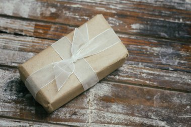 Kahverengi el sanatları kağıdına sarılı bir hediye kutusu ve beyaz saten kurdele. Noel havası. Dekoratif ahşap arka plan. Mevcut paket.