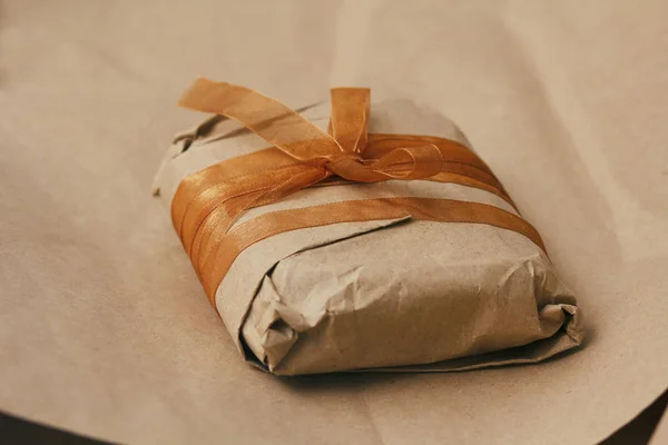 Gift box wrapped in brown craft paper and tie satin ribbon. Christmas mood. Present package. Delivery service. Soft craft pouch.