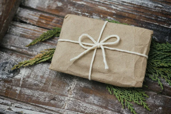 Gift box wrapped in brown craft paper and tie white white string. Christmas mood. Decorative wood background. Present package.Delivery service. Soft craft pouch.