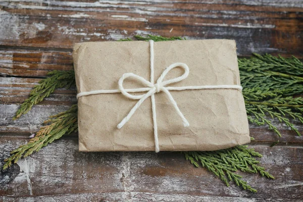 Gift box wrapped in brown craft paper and tie white white string. Christmas mood. Decorative wood background. Present package.Delivery service. Soft craft pouch.