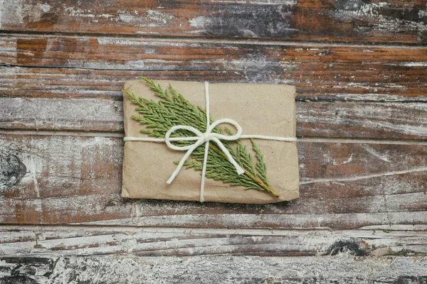 Gift box wrapped in brown craft paper and tie white string. Christmas mood. Decorative wood background. Present package.Delivery service. Soft craft pouch.