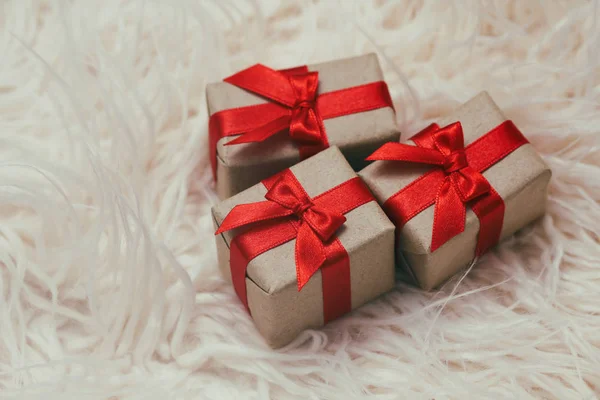 Set of gift boxes wrapped in craft paper and tie red satin ribbon. White fur background. Christmas presents. Holiday mood. New year decor. Gift exchange.
