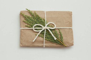 Paket kahverengi el işi kağıdına sarılıp beyaz kurdeleye bağlanmış. Paket var. Teslimat servisi. İnternetten alışveriş. Satın alın. Hediye kutusu masanın üstünde. Beyazda izolasyon. Kozalaklı dal.