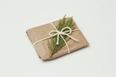 Kahverengi el işi kağıdına sarılı hediye kutusu ve beyaz iplik. Noel havası. Beyaz, sağlam arka plan. Hediye paketi. Kozalaklı dal.