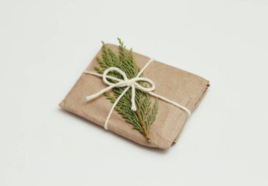 Kahverengi el işi kağıdına sarılı hediye kutusu ve beyaz iplik. Noel havası. Beyaz, sağlam arka plan. Hediye paketi. Kozalaklı dal.