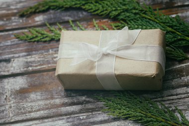 Kahverengi el sanatları kağıdına sarılı bir hediye kutusu ve beyaz saten kurdele. Noel havası. Dekoratif ahşap arka plan. Mevcut paket.