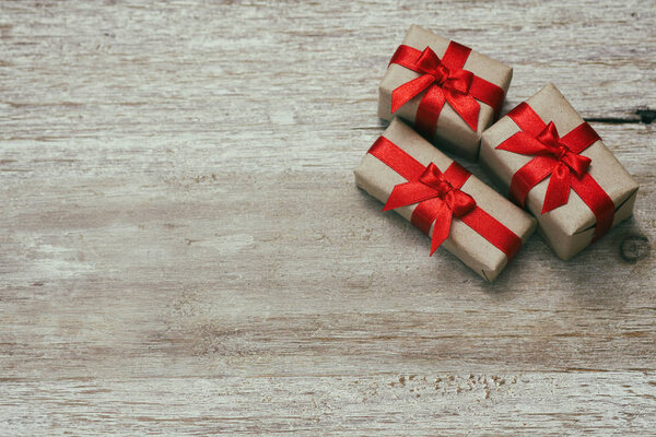 Какие-то подарочные коробки, завернутые в бумагу и завязанные красной атласной лентой. Декоративный деревянный фон. Твоё текстовое пространство. Комплект подарков
.