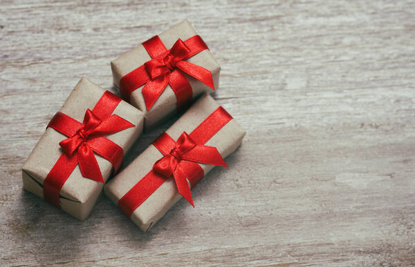 Какие-то подарочные коробки, завернутые в бумагу и завязанные красной атласной лентой. Декоративный деревянный фон. Твоё текстовое пространство. Комплект подарков
.