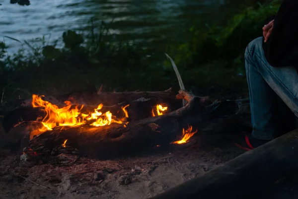 A man sits on a log by the fire. Campfire evening relaxation