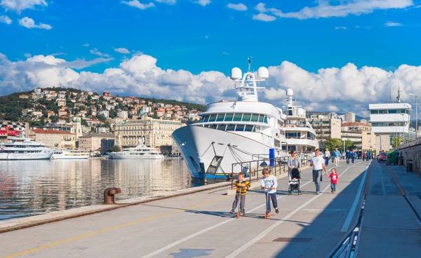 Rijeka, Kroatië: Uitzicht op haven van Rijeka, kinderen rijden scooters op de pier — Stockfoto