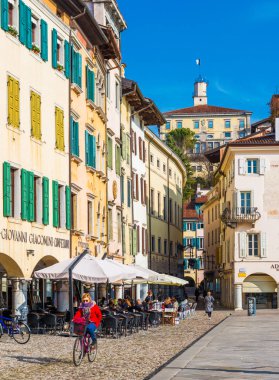 Udine, İtalya: Şehir merkezinde kadın kırmızı ceketli bisiklet olduğunu. Udine sokak renkli evlerin geleneksel mimari tarzı. İnsanlar kafede oturuyor
