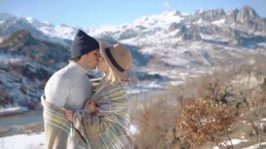 Arka planda güzel karlı dağlarla sarılıp öpüşen genç çift.