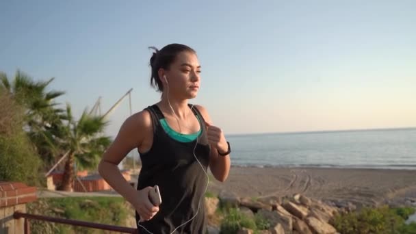 Joggen bij zonsondergang aan het water. Het meisje dat de kust runt. — Stockvideo