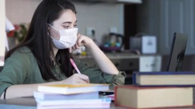 Yüzünde tıbbi maskeyle evde çalışan bir kadın.