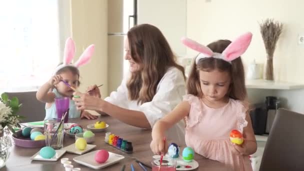 Família feliz que se prepara para a Páscoa. mãe com filhas com orelhas de coelho engraçado pintando ovos de Páscoa juntos, 4K . — Vídeo de Stock