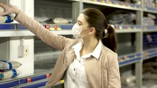 Menina com máscara médica andando ao redor do mercado, empurrando carrinho completo — Vídeo de Stock