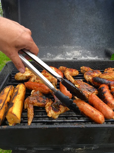 Mano con pinza che mette una salsiccia sulla griglia — Foto Stock