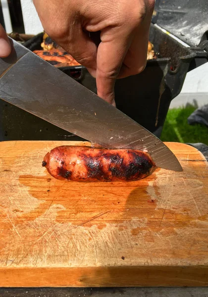 Mano con coltello che taglia una salsiccia su una tavola di legno — Foto Stock