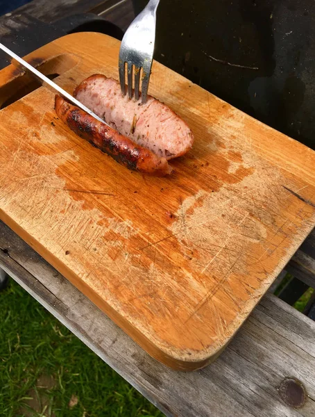 Рука с ножом режет колбасу на деревянной доске — стоковое фото