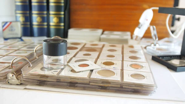 Round magnifying glass on album with coins from different countries - Numismatic scene — Stock Photo, Image