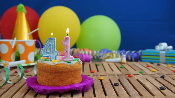 Renkli Balonlar, hediyeler, plastik bardak ve şeker ile mavi duvar arka planda arka plan rustik ahşap masada mumlarla doğum günü pastası. Kek üzerine odaklanmıştır — Stok fotoğraf