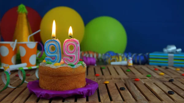 Gâteau d'anniversaire avec des bougies sur table en bois rustique avec fond de ballons colorés, cadeaux, tasses en plastique et bonbons avec mur bleu en arrière-plan. L'accent est mis sur gâteau — Photo