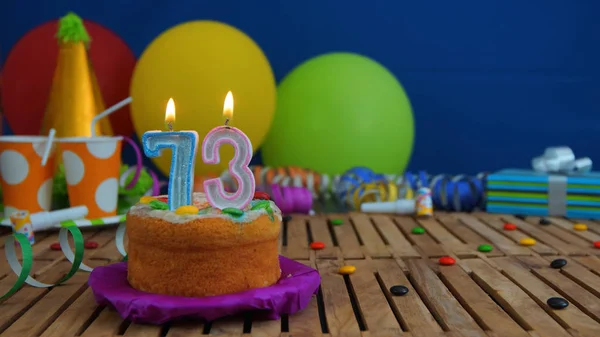 Geburtstagstorte mit Kerzen auf rustikalem Holztisch mit Hintergrund aus bunten Luftballons, Geschenken, Plastikbechern und Bonbons mit blauer Wand im Hintergrund. Fokus liegt auf Kuchen — Stockfoto