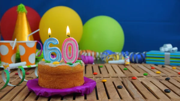 Geburtstagstorte mit Kerzen auf rustikalem Holztisch mit Hintergrund aus bunten Luftballons, Geschenken, Plastikbechern und Bonbons mit blauer Wand im Hintergrund. Fokus liegt auf Kuchen — Stockfoto